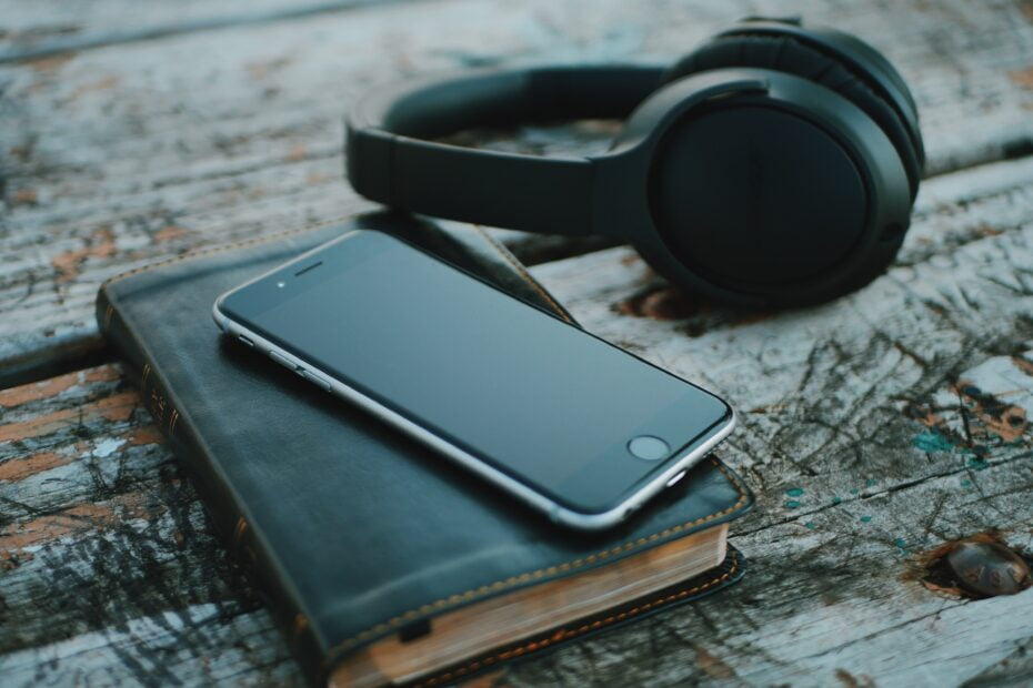 Black smartphone on black diary, over-ear headphones off to the side, on scratched wood slat table. Using as audiobook image