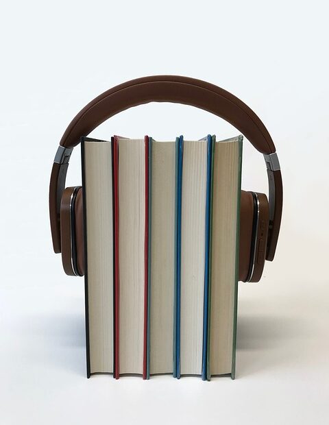 black over ear headphones placed over 5 standing books. Used as an audiobook post image.