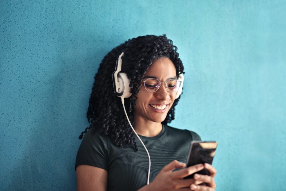 smiling african american woman with white over ear earphones listening to audiobooks.