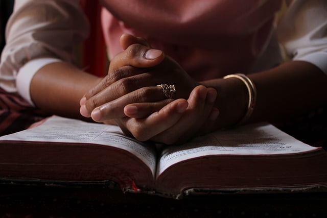 african american person praying with hands clasped on bible, used as image for christianity audiobooks