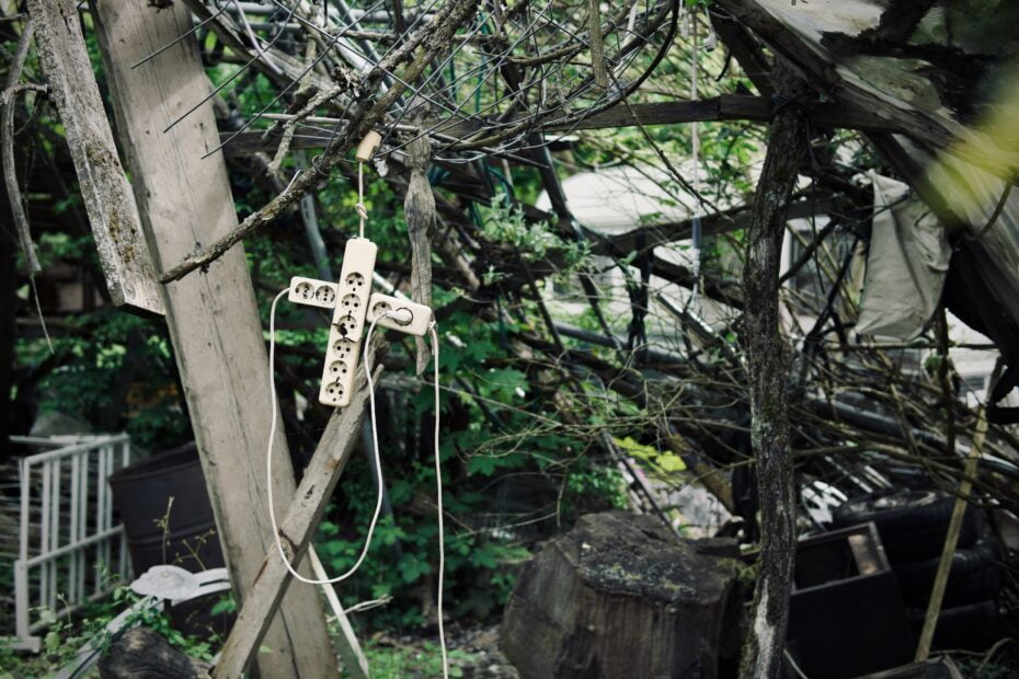 Two white power cords plugged into each other to form cross for occult horror shrine in a overgrown woods setting